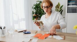 Seorang wanita tengah fokus menghitung dan merencanakan keuangan pribadinya di rumah, menunjukkan komitmen terhadap pengelolaan finansial yang bijak dan terencana untuk masa depan.