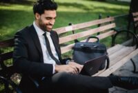 Seorang profesional tampak tersenyum lega setelah menutup laptopnya, di sampingnya ada cangkir kopi dan buku yang siap menemaninya menikmati waktu pribadi. Gambar ini merefleksikan pentingnya membatasi jam kerja untuk meraih keseimbangan hidup yang optimal.