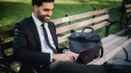Seorang profesional tampak tersenyum lega setelah menutup laptopnya, di sampingnya ada cangkir kopi dan buku yang siap menemaninya menikmati waktu pribadi. Gambar ini merefleksikan pentingnya membatasi jam kerja untuk meraih keseimbangan hidup yang optimal.