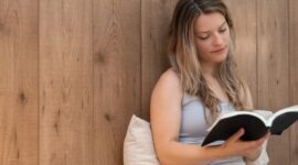 Seorang wanita menikmati momen tenang membaca buku di rumah, menunjukkan pentingnya meluangkan waktu untuk diri sendiri demi menjaga kesehatan mental di tengah kesibukan. Suasana nyaman ini mencerminkan ide me time yang efektif tanpa perlu keluar dari hunian pribadi.