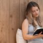 Seorang wanita menikmati momen tenang membaca buku di rumah, menunjukkan pentingnya meluangkan waktu untuk diri sendiri demi menjaga kesehatan mental di tengah kesibukan. Suasana nyaman ini mencerminkan ide me time yang efektif tanpa perlu keluar dari hunian pribadi.