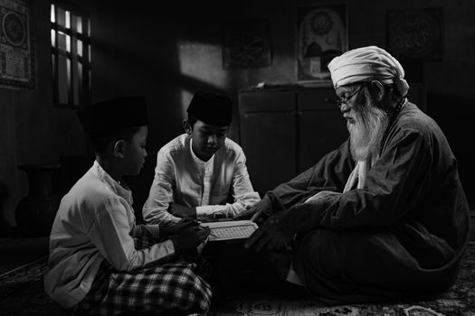 Seorang nenek yang penuh kasih sedang membacakan cerita rakyat Indonesia kepada cucunya, menggambarkan transmisi kearifan lokal dari generasi ke generasi di tengah keindahan tradisi. Gambar ini menangkap esensi kehangatan keluarga dan pentingnya melestarikan warisan budaya melalui kisah-kisah yang tak lekang oleh waktu.