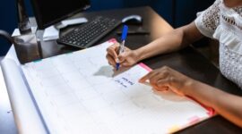 Seorang wanita sedang menyusun jadwal dan daftar prioritas dalam buku catatan, menunjukkan komitmennya terhadap manajemen waktu yang efektif untuk mencapai keseimbangan hidup. Gambar ini merefleksikan upaya proaktif dalam merencanakan hari demi produktivitas yang berkelanjutan.