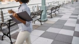 Seorang wanita terlihat sedang menikmati momen tenang sambil minum kopi di balkon, dengan pemandangan kota di kejauhan, menggambarkan pentingnya jeda dan relaksasi di tengah kesibukan. Gambar ini merefleksikan bagaimana menciptakan ruang pribadi untuk mengisi ulang energi adalah kunci untuk mencapai keseimbangan hidup yang lebih baik.