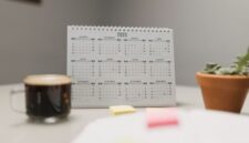 Seorang wanita tengah merencanakan jadwal hariannya menggunakan kalender dan catatan, menunjukkan dedikasi pada manajemen waktu yang terstruktur. Gambar ini merepresentasikan pentingnya perencanaan dan fokus dalam mencapai produktivitas maksimal.