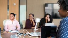 Seorang wanita profesional berdiskusi dengan mentornya di lingkungan kantor modern, menunjukkan kolaborasi dan dukungan dalam pengembangan karier. Gambar ini merepresentasikan pentingnya bimbingan dan pembelajaran berkelanjutan bagi wanita dalam meraih sukses.