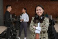 Seorang wanita profesional Indonesia berinteraksi dengan rekan kerja di lingkungan kantor modern, menunjukkan semangat kolaborasi dan kepercayaan diri dalam meniti karier. Suasana dinamis ini merefleksikan pentingnya interaksi positif dan dukungan tim dalam mencapai tujuan profesional.