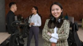Seorang wanita profesional Indonesia berinteraksi dengan rekan kerja di lingkungan kantor modern, menunjukkan semangat kolaborasi dan kepercayaan diri dalam meniti karier. Suasana dinamis ini merefleksikan pentingnya interaksi positif dan dukungan tim dalam mencapai tujuan profesional.