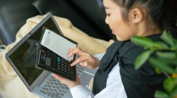 Seorang perempuan Indonesia dengan penuh konsentrasi memeriksa laporan keuangan di laptopnya, merefleksikan dedikasi dalam mengelola masa depan finansialnya. Gambar ini menunjukkan kemandirian dan kecakapan perempuan dalam mengambil kendali atas keputusan keuangannya.