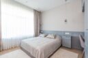 Kamar tidur minimalis dengan dominasi warna netral dan pencahayaan alami yang melimpah, menciptakan suasana tenang dan lapang. Desain ini mengutamakan fungsi esensial dan keindahan sederhana untuk mendukung istirahat yang berkualitas.
