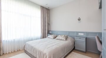 Kamar tidur minimalis dengan dominasi warna netral dan pencahayaan alami yang melimpah, menciptakan suasana tenang dan lapang. Desain ini mengutamakan fungsi esensial dan keindahan sederhana untuk mendukung istirahat yang berkualitas.