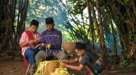 Seorang nenek mendongeng kepada cucu-cucunya di teras rumah pedesaan, menggambarkan tradisi lisan yang masih hidup di banyak daerah Indonesia. Momen hangat ini menunjukkan bagaimana cerita rakyat diwariskan secara personal dari generasi ke generasi.