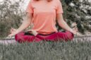 Seorang wanita sedang bermeditasi dengan tenang di tengah hijaunya alam, merefleksikan esensi gaya hidup "slow living" yang menenangkan jiwa dan pikiran dari hiruk pikuk kehidupan. Pemandangan ini menggambarkan ketenangan serta keseimbangan yang bisa dicapai melalui kesadaran penuh terhadap diri sendiri dan lingkungan sekitar.