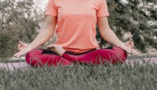 Seorang wanita sedang bermeditasi dengan tenang di tengah hijaunya alam, merefleksikan esensi gaya hidup "slow living" yang menenangkan jiwa dan pikiran dari hiruk pikuk kehidupan. Pemandangan ini menggambarkan ketenangan serta keseimbangan yang bisa dicapai melalui kesadaran penuh terhadap diri sendiri dan lingkungan sekitar.