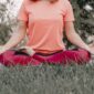 Seorang wanita sedang bermeditasi dengan tenang di tengah hijaunya alam, merefleksikan esensi gaya hidup "slow living" yang menenangkan jiwa dan pikiran dari hiruk pikuk kehidupan. Pemandangan ini menggambarkan ketenangan serta keseimbangan yang bisa dicapai melalui kesadaran penuh terhadap diri sendiri dan lingkungan sekitar.