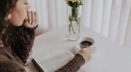 Seorang wanita menikmati secangkir teh hangat sambil membaca buku di sofa yang nyaman, menciptakan momen *me time* yang tenang dan menenangkan di tengah kesibukan hari. Gambar ini merefleksikan pentingnya jeda untuk diri sendiri demi menjaga keseimbangan hidup.
