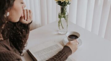 Seorang wanita menikmati secangkir teh hangat sambil membaca buku di sofa yang nyaman, menciptakan momen *me time* yang tenang dan menenangkan di tengah kesibukan hari. Gambar ini merefleksikan pentingnya jeda untuk diri sendiri demi menjaga keseimbangan hidup.