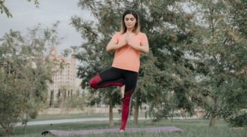 Sebuah piring berisi makanan sehat berwarna-warni di samping seseorang yang sedang melakukan yoga di taman, menggambarkan keseimbangan antara nutrisi dan aktivitas fisik untuk hidup yang lebih sehat.